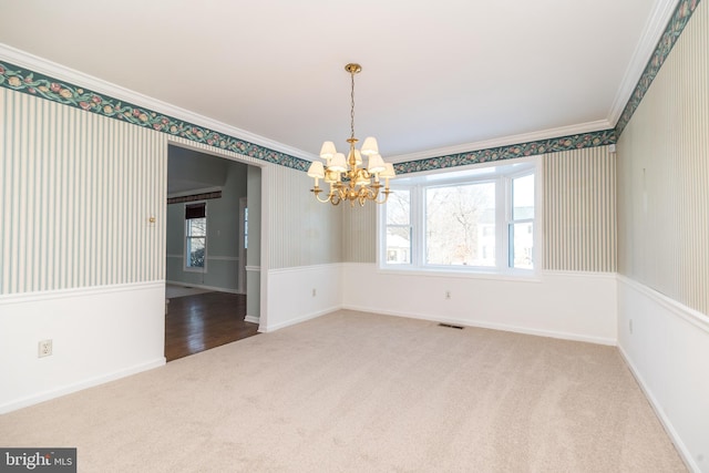 spare room featuring an inviting chandelier, crown molding, and carpet