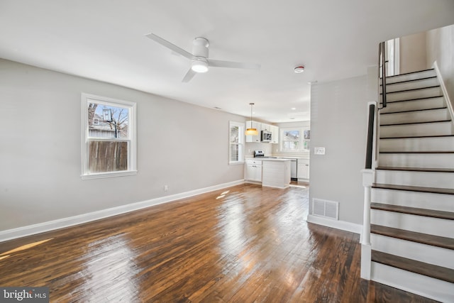 unfurnished living room with visible vents, baseboards, a ceiling fan, wood-type flooring, and stairway