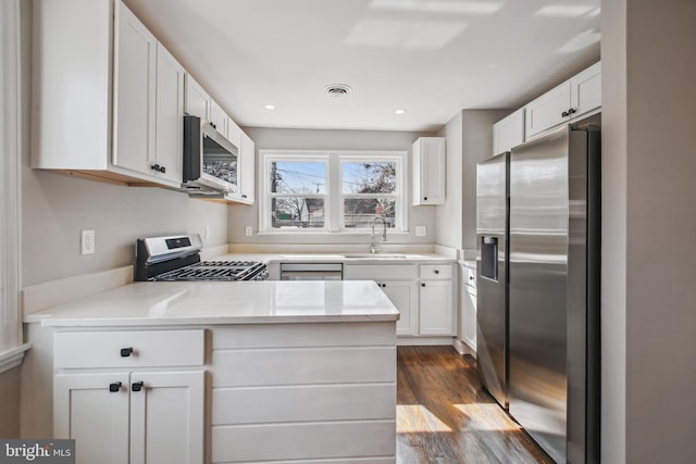 kitchen with stainless steel appliances, visible vents, dark wood-type flooring, white cabinetry, and a sink