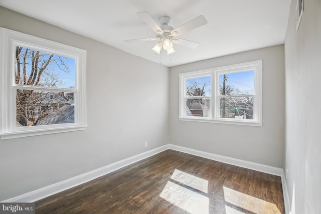 spare room with dark wood-type flooring, visible vents, ceiling fan, and baseboards