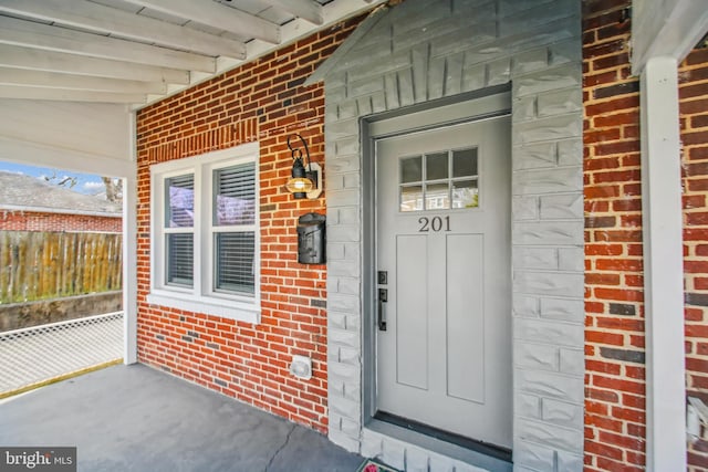 entrance to property with a porch, brick siding, and fence