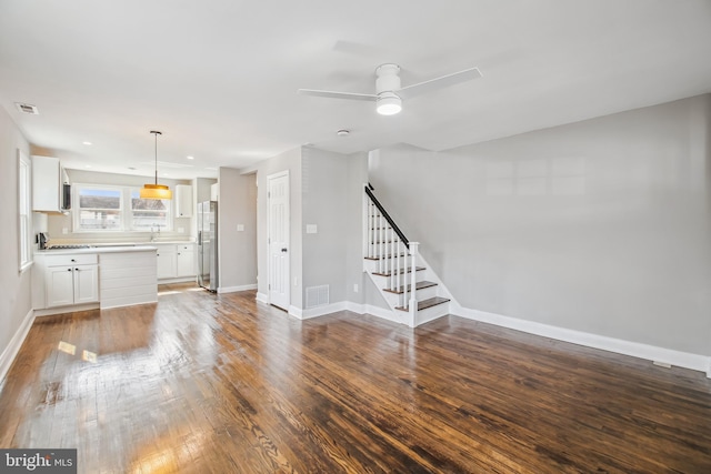 unfurnished living room featuring baseboards, visible vents, stairway, dark wood-type flooring, and a sink