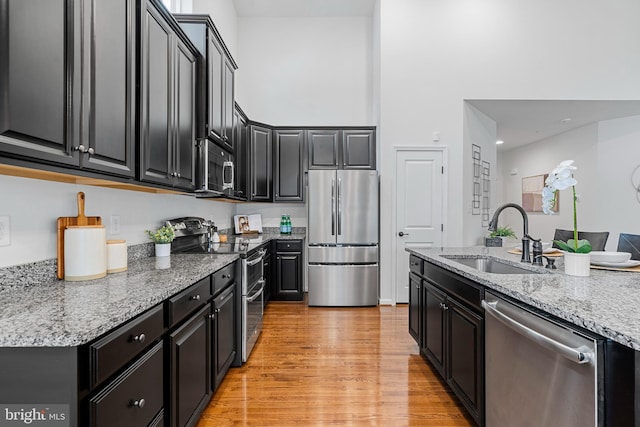 kitchen with sink, stainless steel appliances, light stone counters, and light hardwood / wood-style floors