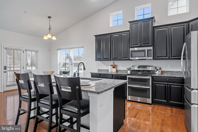 kitchen with appliances with stainless steel finishes, a kitchen bar, dark stone countertops, sink, and a kitchen island with sink