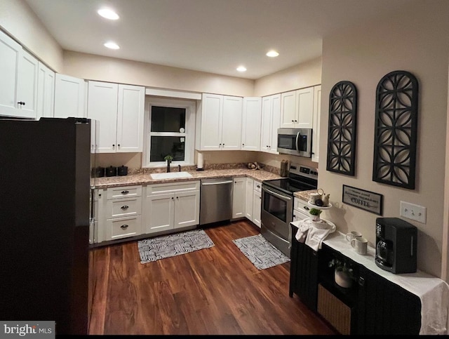 kitchen with dark hardwood / wood-style floors, sink, white cabinetry, light stone countertops, and appliances with stainless steel finishes