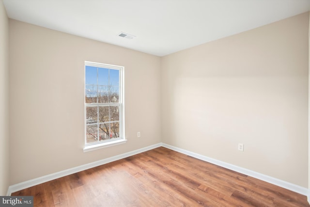 empty room with wood finished floors, visible vents, and baseboards