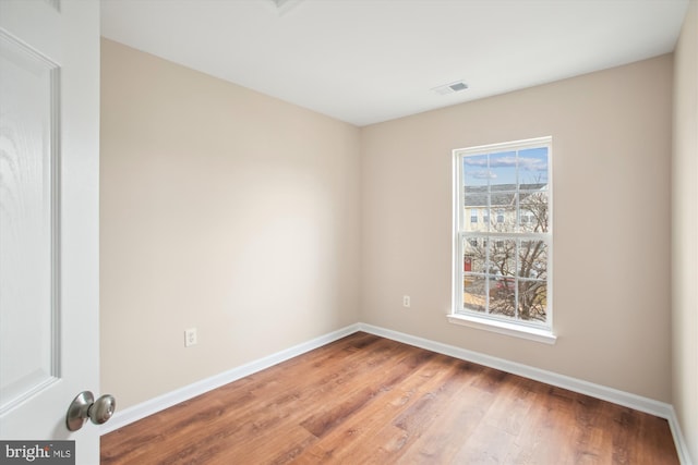 spare room with baseboards, visible vents, and wood finished floors