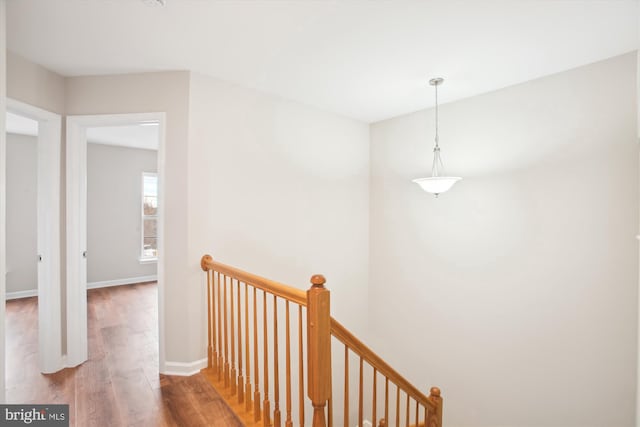 corridor featuring baseboards, wood finished floors, and an upstairs landing