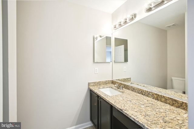 bathroom featuring toilet, vanity, visible vents, and baseboards