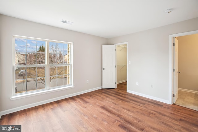 unfurnished bedroom with multiple windows, visible vents, baseboards, and wood finished floors