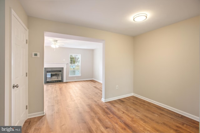 unfurnished living room with a fireplace with flush hearth, light wood-style flooring, baseboards, and a ceiling fan