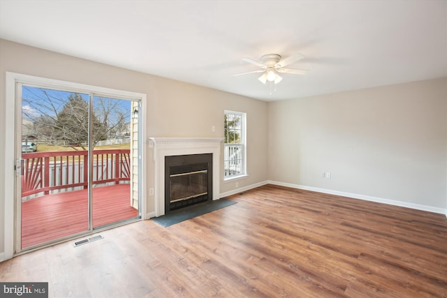 unfurnished living room featuring wood finished floors, a ceiling fan, visible vents, baseboards, and a glass covered fireplace