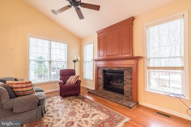 living area featuring vaulted ceiling, a brick fireplace, light hardwood / wood-style flooring, and ceiling fan