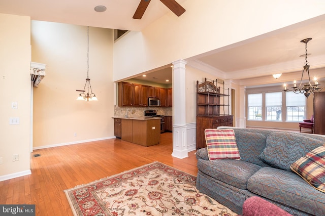 living room with light wood-type flooring, crown molding, ceiling fan with notable chandelier, and decorative columns