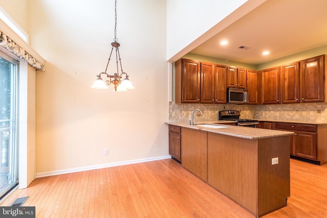 kitchen featuring decorative light fixtures, light hardwood / wood-style floors, kitchen peninsula, sink, and appliances with stainless steel finishes