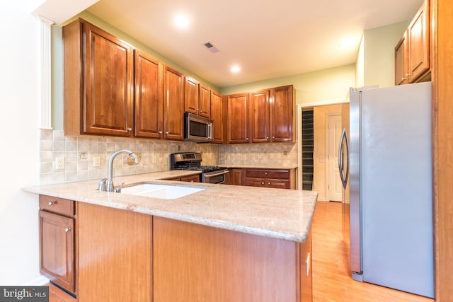 kitchen featuring light stone countertops, kitchen peninsula, sink, and stainless steel appliances