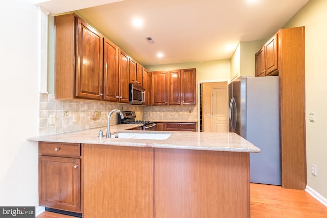 kitchen featuring kitchen peninsula, light stone countertops, stainless steel appliances, and light hardwood / wood-style floors