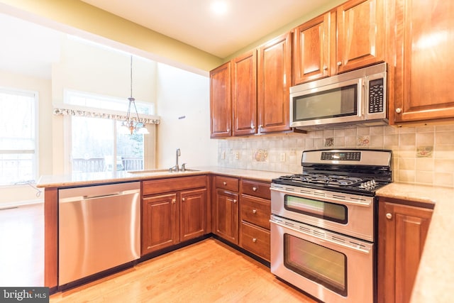 kitchen featuring appliances with stainless steel finishes, decorative backsplash, light wood-type flooring, hanging light fixtures, and sink