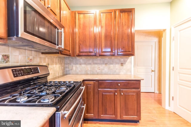 kitchen with tasteful backsplash, light wood-type flooring, appliances with stainless steel finishes, and light stone counters