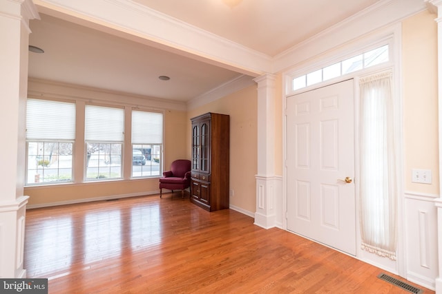 foyer with light hardwood / wood-style flooring, crown molding, and ornate columns