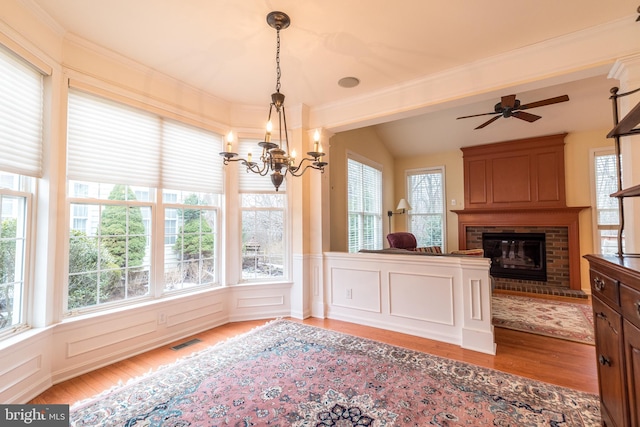 dining space with light hardwood / wood-style floors, ceiling fan with notable chandelier, and a fireplace