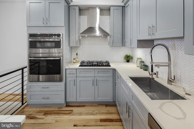 kitchen featuring black gas stovetop, wall chimney range hood, double oven, tasteful backsplash, and sink