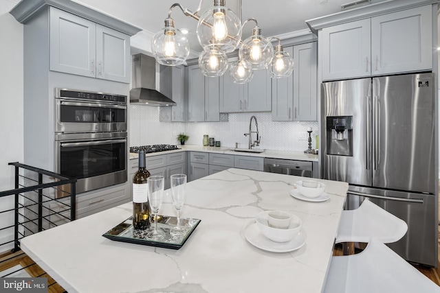 kitchen with appliances with stainless steel finishes, wall chimney range hood, tasteful backsplash, sink, and light stone counters