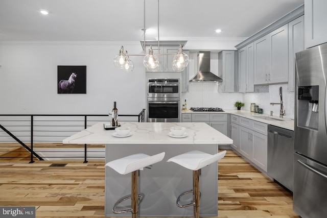 kitchen featuring a kitchen island, wall chimney range hood, stainless steel appliances, sink, and hanging light fixtures