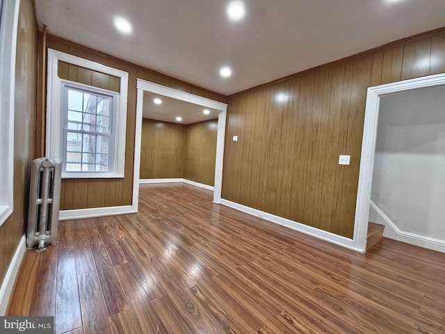 unfurnished room with hardwood / wood-style flooring, radiator, and wood walls