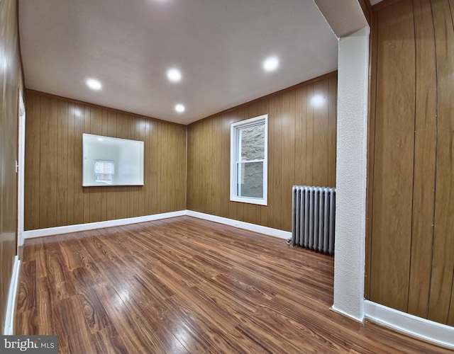 spare room featuring dark wood-type flooring, wood walls, and radiator heating unit