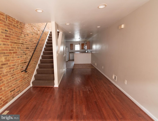 unfurnished living room with brick wall and dark hardwood / wood-style floors