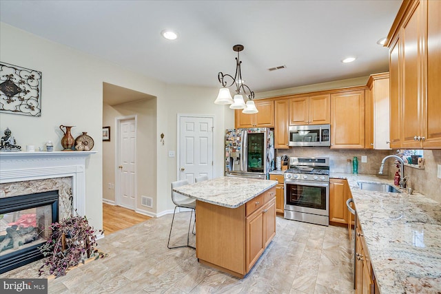 kitchen with a kitchen island, sink, stainless steel appliances, a high end fireplace, and light stone counters