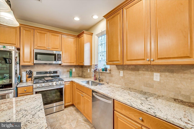 kitchen featuring light stone countertops, appliances with stainless steel finishes, backsplash, and sink