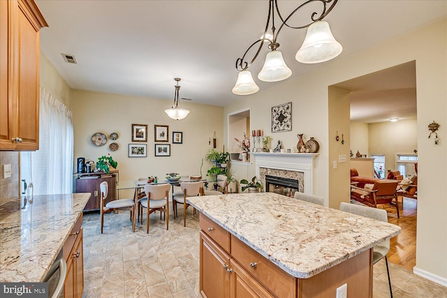 kitchen with light stone countertops, pendant lighting, a high end fireplace, a center island, and a breakfast bar