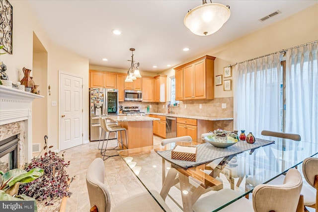 kitchen featuring stainless steel appliances, backsplash, hanging light fixtures, light stone countertops, and a center island