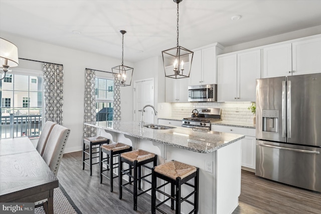 kitchen with sink, appliances with stainless steel finishes, pendant lighting, a kitchen island with sink, and white cabinets