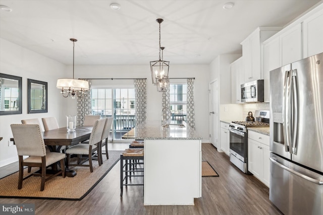 kitchen with light stone counters, hanging light fixtures, white cabinets, and appliances with stainless steel finishes