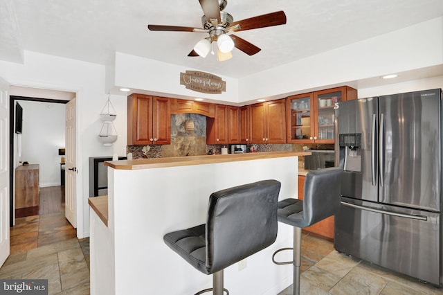 kitchen with stainless steel refrigerator with ice dispenser, a breakfast bar area, backsplash, and ceiling fan