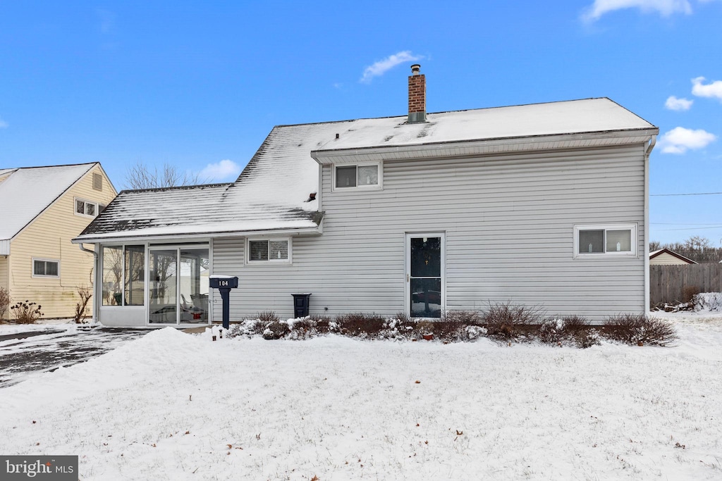 snow covered rear of property featuring a sunroom