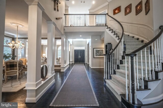 entryway with a notable chandelier, crown molding, decorative columns, and dark hardwood / wood-style floors