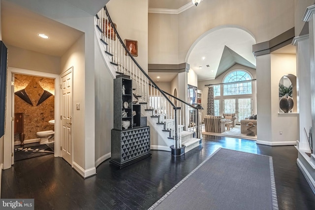 foyer with ornamental molding, a towering ceiling, and dark wood-type flooring