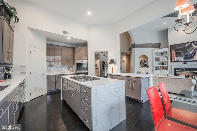 kitchen featuring a kitchen island, appliances with stainless steel finishes, tasteful backsplash, dark hardwood / wood-style flooring, and kitchen peninsula