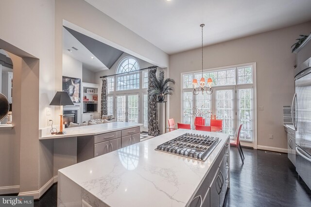 kitchen with hanging light fixtures, light stone countertops, stainless steel gas cooktop, and a wealth of natural light