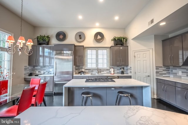 kitchen with hanging light fixtures, stainless steel built in refrigerator, a kitchen island, and light stone counters