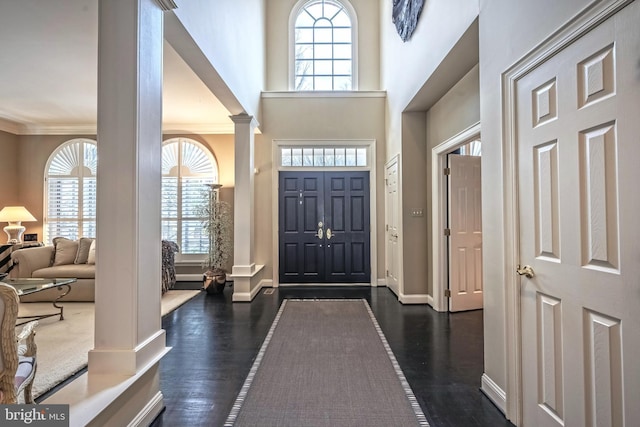 foyer with decorative columns, ornamental molding, plenty of natural light, and dark wood-type flooring