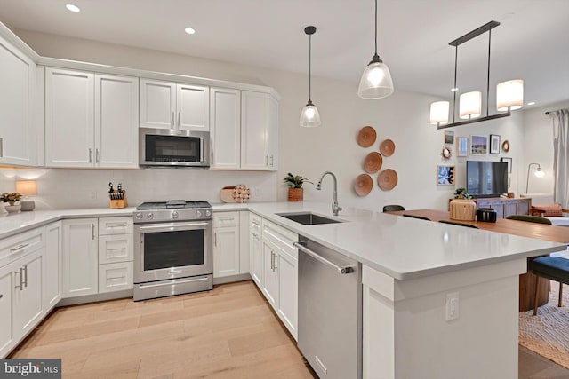 kitchen with kitchen peninsula, stainless steel appliances, hanging light fixtures, white cabinets, and sink