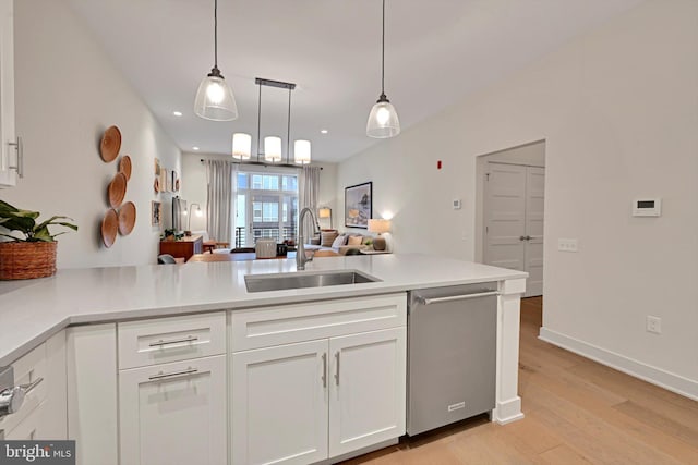 kitchen featuring decorative light fixtures, stainless steel dishwasher, kitchen peninsula, sink, and white cabinetry