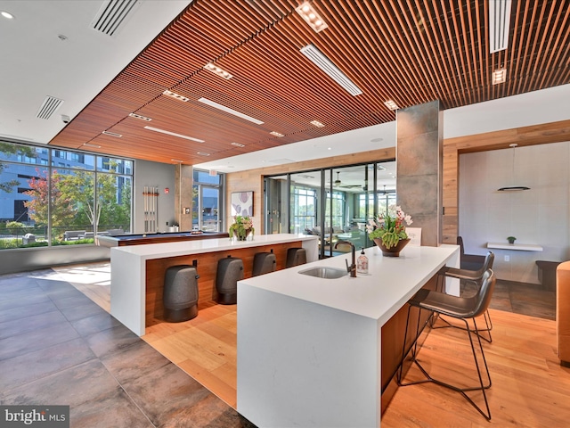 kitchen featuring sink, expansive windows, wood ceiling, an island with sink, and a breakfast bar area