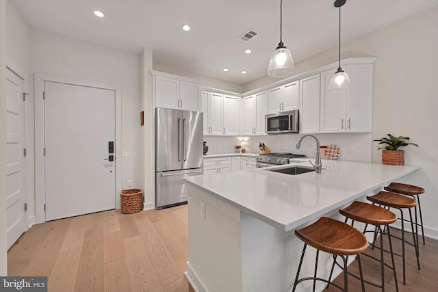 kitchen featuring a kitchen bar, appliances with stainless steel finishes, hanging light fixtures, white cabinets, and sink