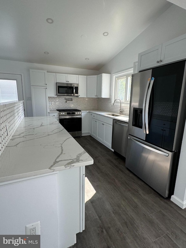 kitchen with vaulted ceiling, appliances with stainless steel finishes, white cabinetry, sink, and light stone countertops